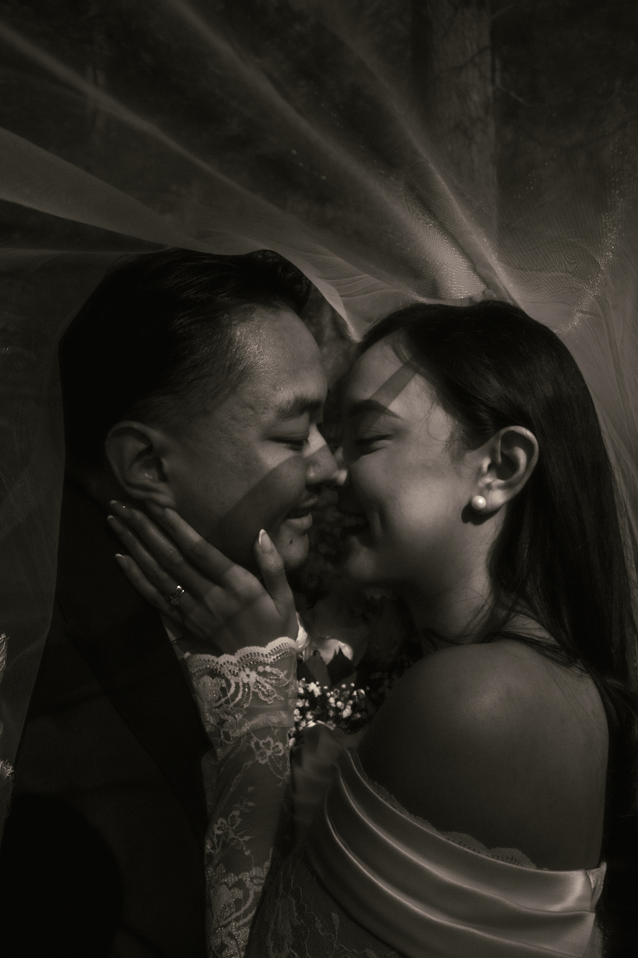 Bride and groom smiling beneath a veil in a dramatic monochrome portrait