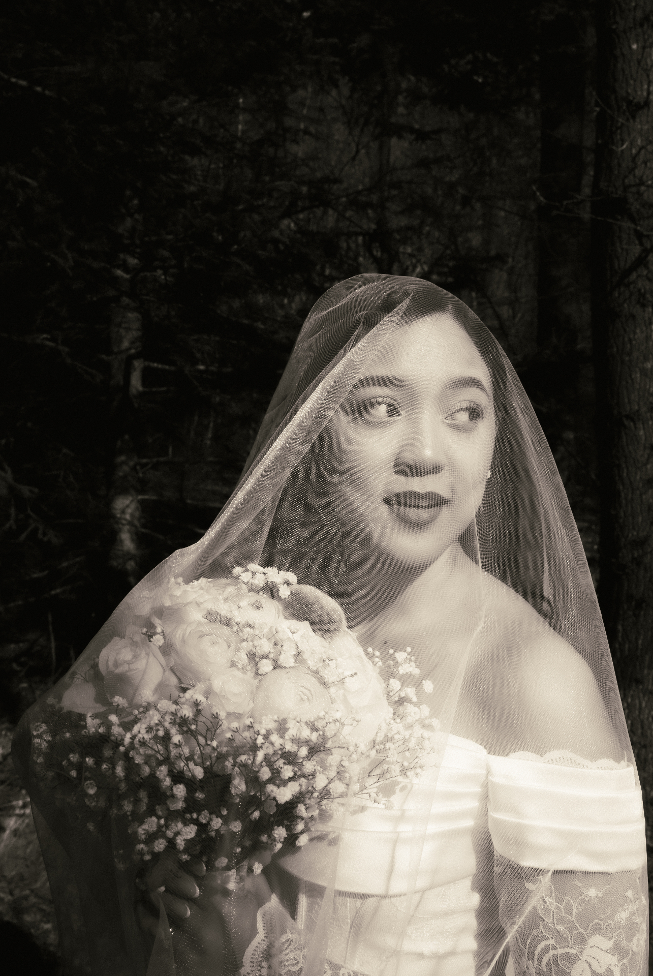 Bride holding a bouquet beneath her veil in a black and white portrait